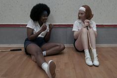 two women sitting on the floor with tennis rackets in their hands and one holding a bat