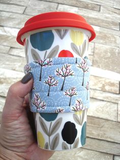 a hand holding a coffee cup in front of a brick wall with trees on it