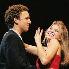 a man and woman standing next to each other with their arms around each other, smiling