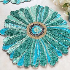 two pieces of blue and green beaded jewelry on a white surface with flowers in the background