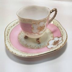 a cup and saucer sitting on top of a pink plate with gold trimmings