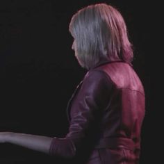 a woman standing in front of a black background wearing a red leather jacket and holding her hand out