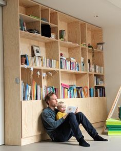 a man sitting on the floor reading a book next to a ladder and bookshelf