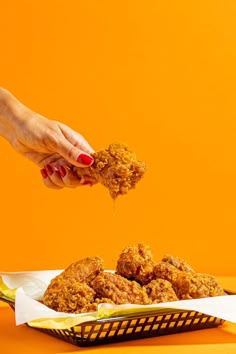 a person is scooping some food out of a paper basket on an orange background