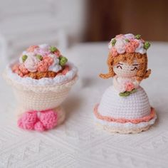 two small crocheted dolls sitting on top of a white table covered in doily