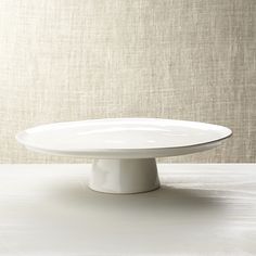 a white cake plate sitting on top of a table next to a beige cloth wall