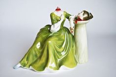 a ceramic figurine of two people dressed in green and white, one holding the other's head