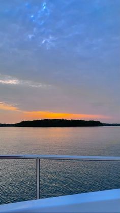 the sun is setting over the water from a boat in the ocean with trees and land behind it