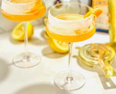 two glasses filled with drinks sitting on top of a table next to lemons and bottles