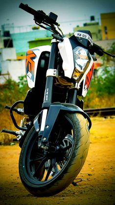 a white and orange motorcycle parked on top of a dirt road next to a building