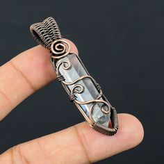 a hand holding a wire wrapped pendant in it's left hand, with an intricate design on the front