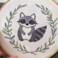 a cross stitch raccoon is sitting in a wreath