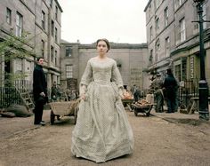 a woman in a long dress walking down the street with two men standing behind her