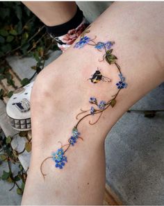 a woman's leg with blue flowers on it and a butterfly tattoo on the side