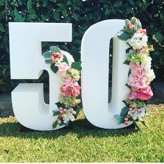 the number 50 is decorated with flowers and greenery in front of a bushy background