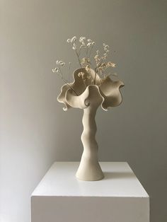 a white vase with flowers in it on top of a table next to a wall