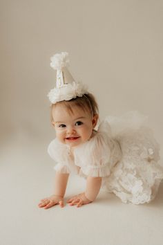 a baby girl wearing a white dress and a party hat