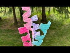 there are three different colored ribbons hanging from a tree branch in the grass and one is pink, blue, and green