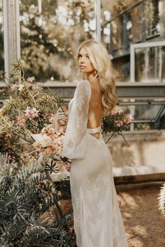 a woman in a white dress standing next to some trees and flowers with her back turned towards the camera