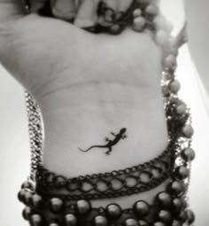 a small lizard tattoo on the wrist with beads around it's neck and foot