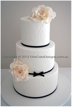 a three tiered wedding cake with white flowers on top and black ribbon around the bottom