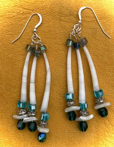 two white and green earrings are hanging on a yellow surface, with beads attached to them