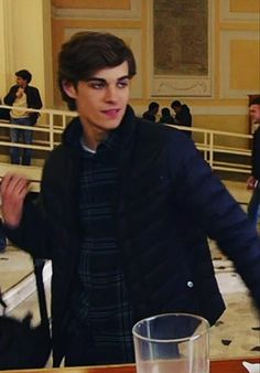 a young man standing in front of a table with a glass on top of it