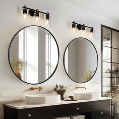 two round mirrors are above the double sinks in this modern bathroom with black cabinetry and marble countertops