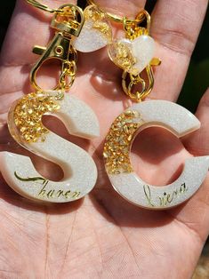 two white and gold earrings with the letter s on them are being held in someone's hand