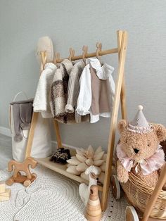 a teddy bear sitting next to a wooden rack with clothes on it's hangers