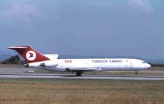 a white and red jet airliner on runway next to grassy area with mountains in the background