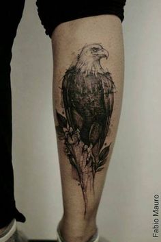 an eagle tattoo on the leg of a woman's leg, with leaves and flowers around it