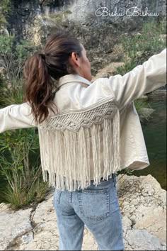 a woman standing on top of a rock next to a river wearing a white jacket