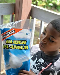 a young boy is holding a bag of gluer planeer on the porch with a straw in his hand