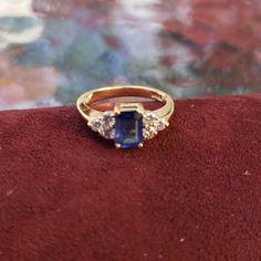 a gold ring with a blue stone surrounded by small diamonds on a red velvet surface