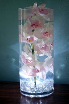 a glass vase filled with pink and white flowers on top of a wooden table next to a wall