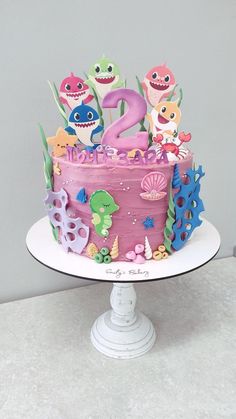 a birthday cake with pink frosting and cartoon characters on it, sitting on a white pedestal