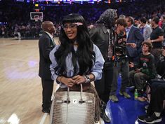 a woman holding a purse standing on top of a basketball court next to other people