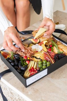 a woman is cutting into a large tray of fruit and cheeses on a table