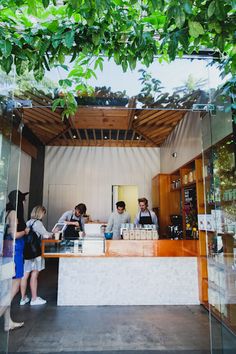 some people are standing at a counter in a building with trees on the roof and glass walls