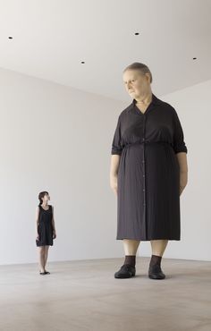 a woman standing next to a large statue in the middle of a room with white walls