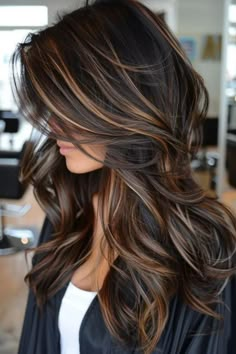 Woman with long, wavy hair featuring brown and blonde highlights in a salon setting. Balayage Hair Blonde To Brown, Black Hair With Golden Brown Highlights, Rich Dark Brown Hair With Highlights, Long Layered Highlighted Hair, Blonde Highlights On Dark Hair Wavy, Hair Lowlights For Brown Hair, Cool Tone Brown Highlights, Hazel Highlights On Dark Hair, Dark Brown Hair With Caramel Highlights And Lowlights