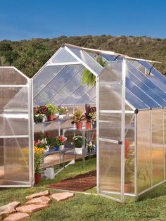 two greenhouses in the grass with plants and flowers growing inside them, on a sunny day