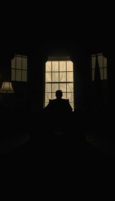 the silhouette of a man sitting in front of a window