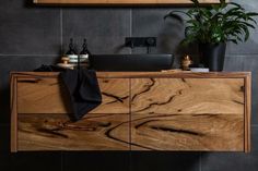 a bathroom vanity with wooden drawers and black tiled walls, along with a potted plant on the counter