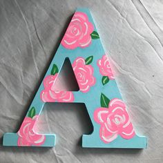 the letter a is decorated with pink roses and green leaves on blue paper, sitting on top of a gray sheet