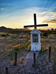 an old cemetery with a wooden cross on top and the sun setting in the background