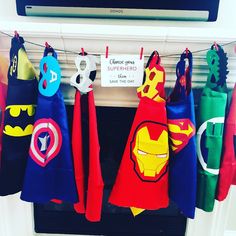 several superhero capes hanging on a clothesline in front of a tv screen with a sign that says,