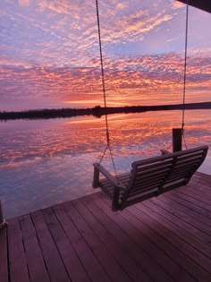 a bench sitting on top of a wooden pier next to the ocean under a colorful sky