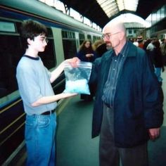 an older man handing something to a young boy on a train platform at a station